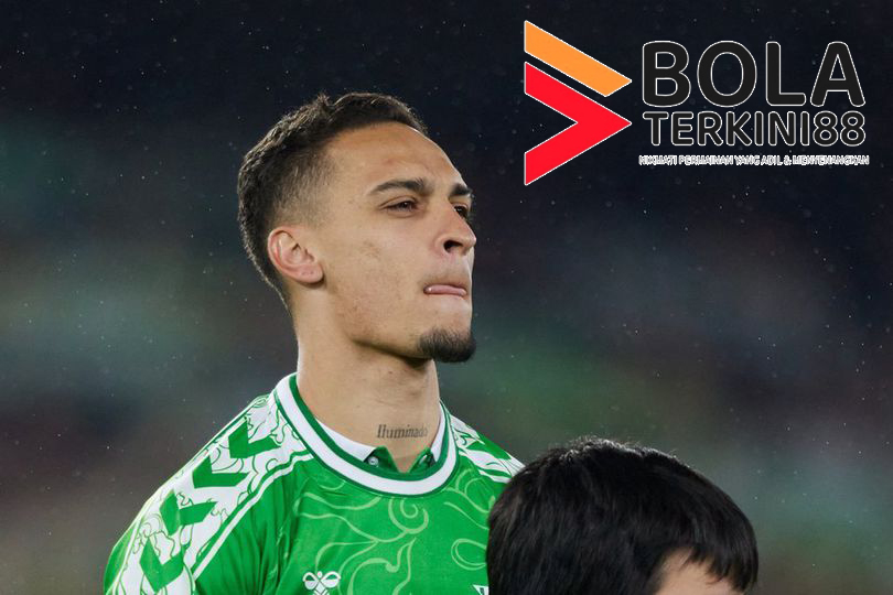 Pemain Real Betis, Antony, mengenakan jersey hijau saat berdiri di lapangan menjelang pertandingan La Liga, dengan logo Bolaterkini88 di sudut gambar.