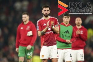 Bruno Fernandes, kapten Manchester United, berdiri di tengah lapangan sambil bertepuk tangan, mengenakan jersey merah dengan logo Bolaterkini88 di pojok kanan atas.